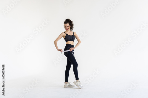 Smiling young woman with beautiful body measuring thigh with measurement type after diet  isolated on white background