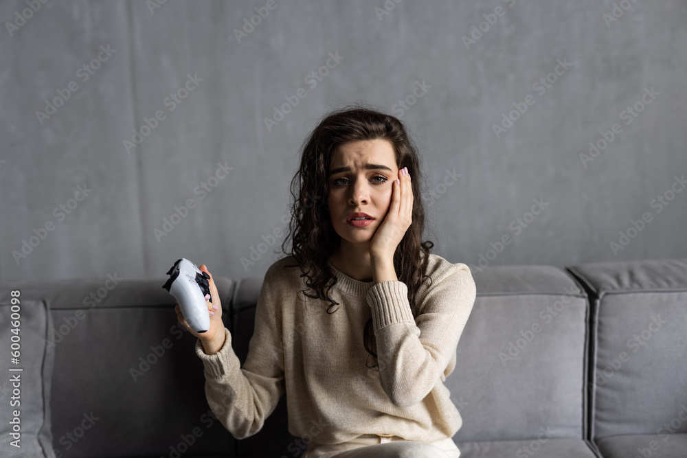 Fototapeta premium Emotional young woman playing video games sit on couch at home