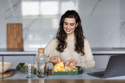 Young woman taking a break and eating pizza  working from home on laptop