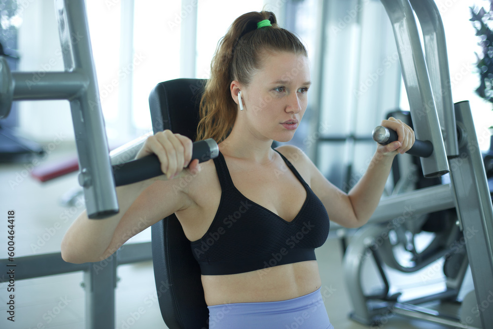 Young fit fitness woman is training at gym doing exercise at machine, listening to music Young fit fitness woman is training at gym doing exercise at machine, listening to music