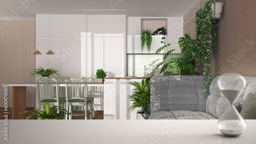 White table or shelf with crystal hourglass measuring the passing time over minimalist dining room and kitchen  sofa  house plant interior design  copy space background