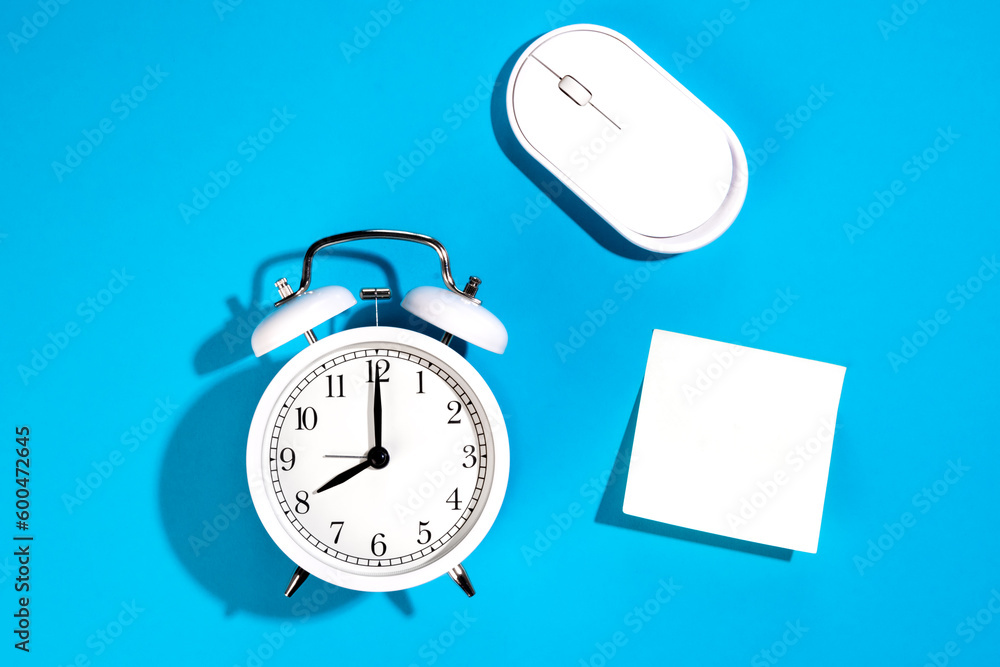 White alarm clock and blank white paper sticker on a blue background isolated. White alarm clock and blank white paper sticker on a blue background isolated.