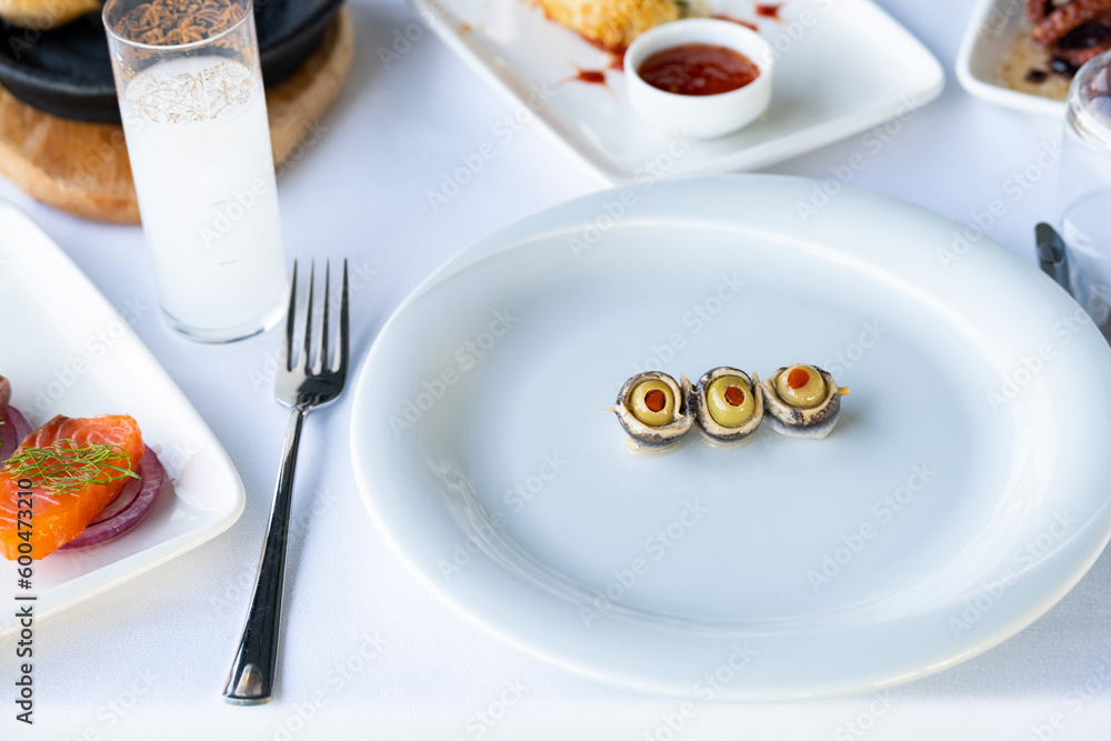 Anchovies wrapped in green olives on the white plate, seafood restaurant, Turkish raki.