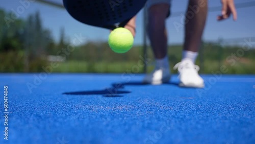 Slow motion of a padel player bounces the ball to pick it up on the court with a racket.