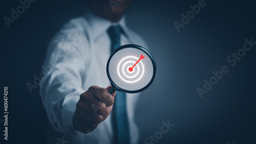 Businessman hand holding a magnifying glass Dart board icon inside, concept of goals and targets achieved, effective business through strategies to achieve the best results of targeted business