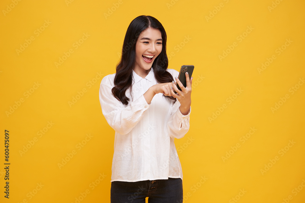 Happy smiling young asian woman using mobile phone isolated on yellow background. teen social media communication online. Happy smiling young asian woman using mobile phone isolated on yellow background. teen social media communication online.