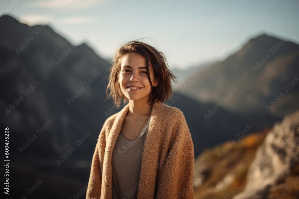 Smiling young woman in the mountains at sunset, looking at camera