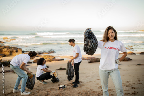 Positive proud young asian lady volunteer with friends in gloves show garbage bag, clean up trash © Prostock-studio