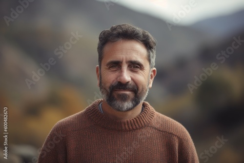 Portrait of a handsome middle-aged man with a beard and mustache in a brown sweater on a background of mountains