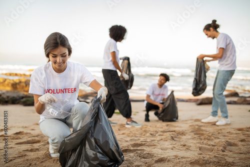 Positive young international people volunteers in gloves and european lady with garbage bags clean up