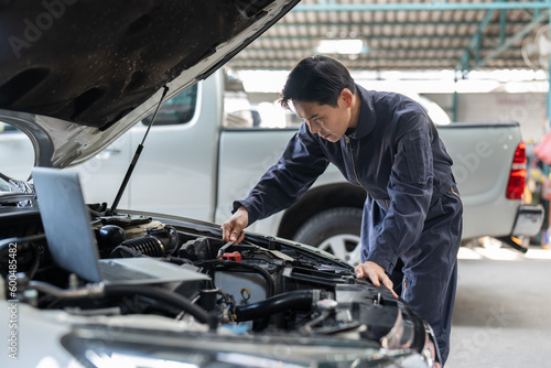 Asian mechanic man using spanner tighten car battery at auto car garage service. Car repair and maintenance concept.