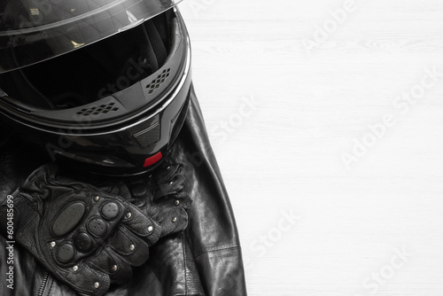 A motorcycle helmet, leather jacket and sport gloves on the white wooden table background with copy space.