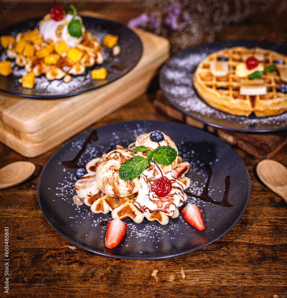 Fototapeta premium Delicious homemade waffles with fresh fruits, ice cream, meringue, strawberry, marshmallow, blueberry, mango, colorful candy, different toppings, banana, jam - sweet food