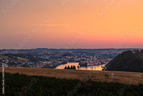 landscape with a woman walking through a wheat field and sunset over the city passau