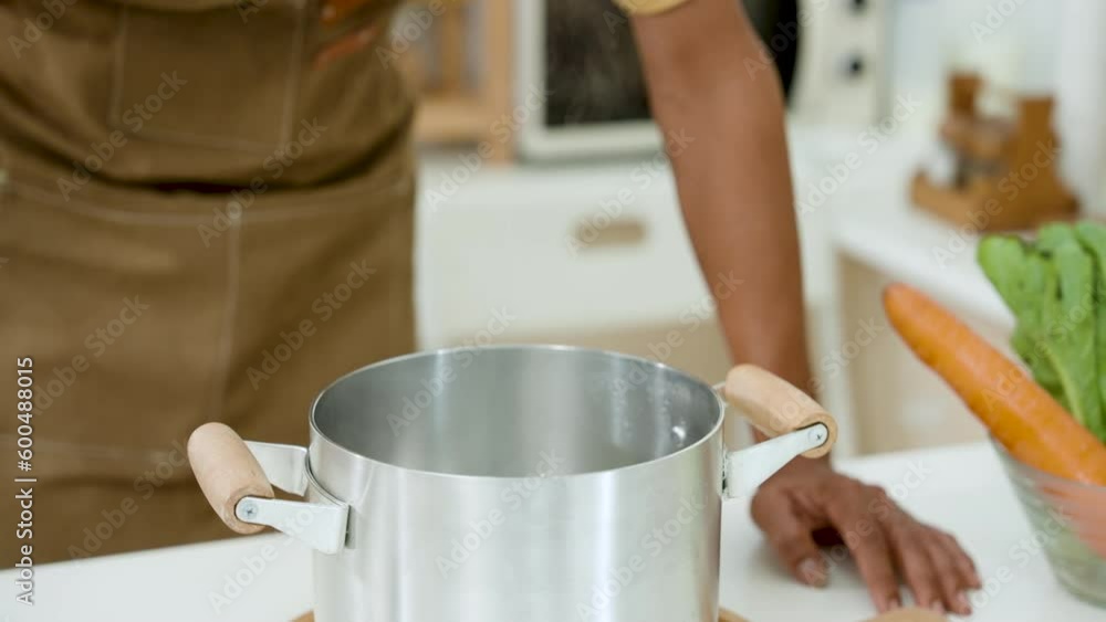 Close-up shot of a man's hand wearing a heat resistant glove Use a ladle to stir the hot soup in the pot. Dressed in an apron preparing dinner, in the kitchen On days when you have to stay home alone Close-up shot of a man's hand wearing a heat resistant glove Use a ladle to stir the hot soup in the pot. Dressed in an apron preparing dinner, in the kitchen On days when you have to stay home alone