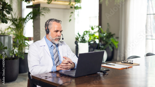 Senior caucasian doctor online video call conference consult patient with headset on laptop computer. Doctor online consultation and telehealth medicine