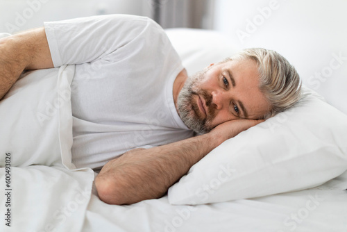 Upset grey-haired man lying in bed in the morning