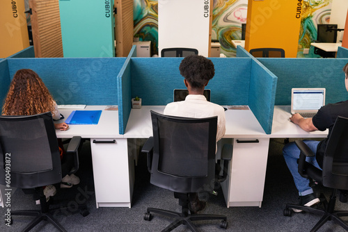 Three young people share coworking space, work side by side with desk dividers