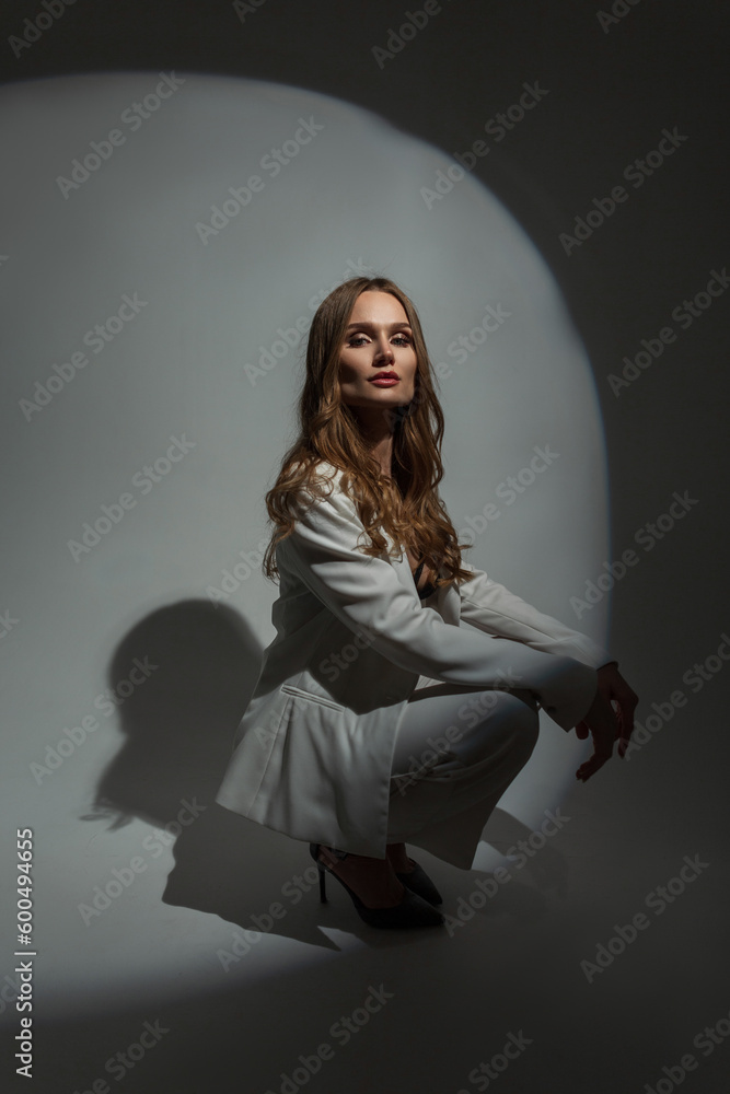 Fashionable beautiful stylish woman model in fashion white suit with blazer sitting and posing in studio on dark background Fashionable beautiful stylish woman model in fashion white suit with blazer sitting and posing in studio on dark background