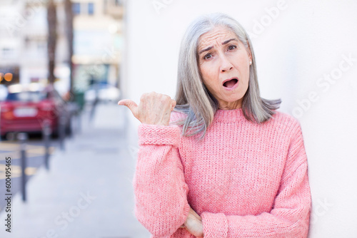 senior retired pretty white hair woman looking astonished in disbelief, pointing at object on the side and saying wow, unbelievable