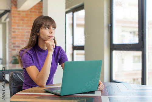 young pretty woman smiling with a happy, confident expression with hand on chin. desk laptop concept