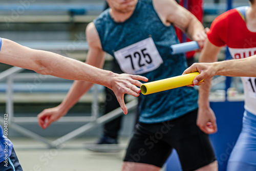 men relay race baton passing in summer athletics championship, close-up of athletes hands on background of runners photo