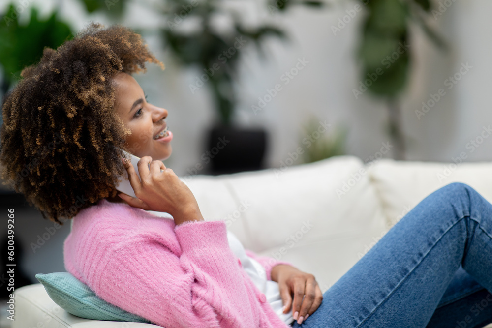 Relaxed young black lady reclining on couch, talking on phone Relaxed young black lady reclining on couch, talking on phone