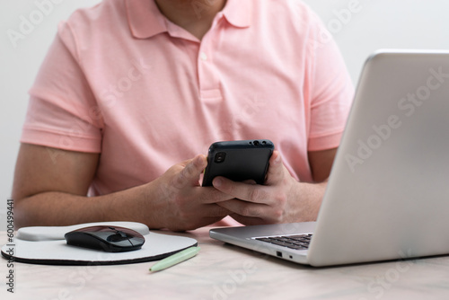 Close up of student using his cell phone front their laptop in white background