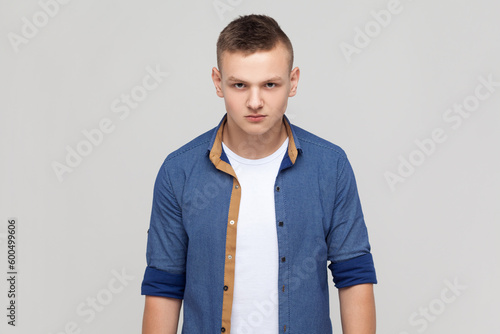Fotografi Portrait of enraged furious attractive teenager boy wearing blue shirt standing looking at camera, expressing wild anger and hate, feeling crazy