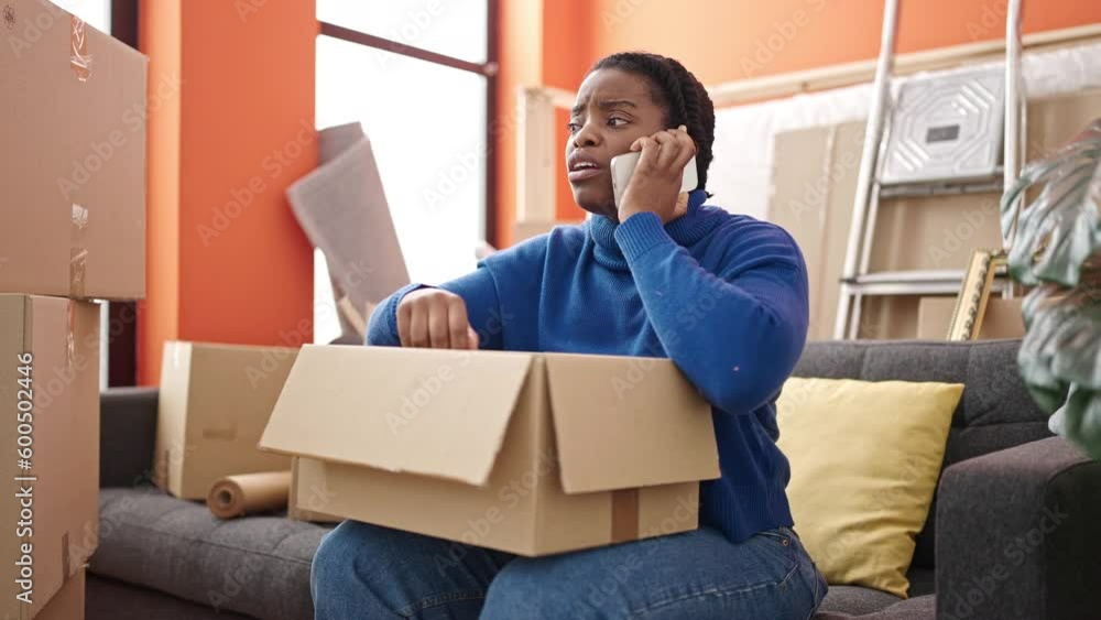 African american woman speaking on the phone unpacking cardboard box at new home African american woman speaking on the phone unpacking cardboard box at new home