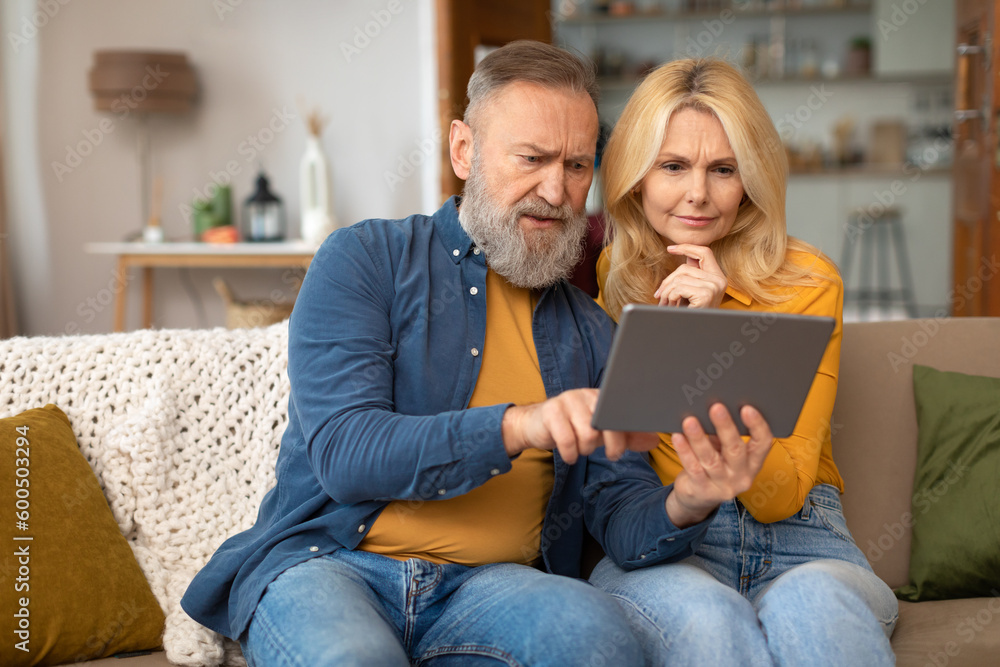 Puzzled Senior Couple Using Digital Tablet Browsing Internet At Home