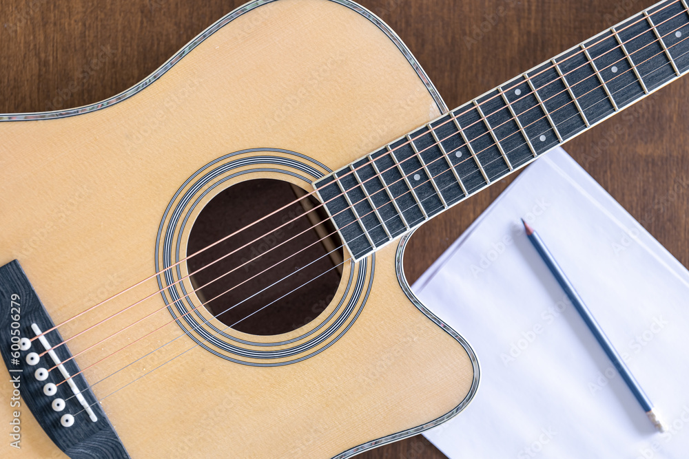 Guitar, sheet of paper and pencil on a wooden background, top view.