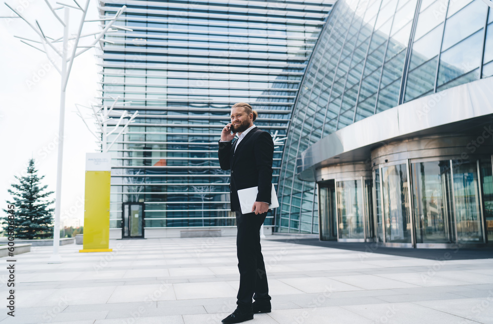 Positive businessman talking on smartphone over modern office building Positive businessman talking on smartphone over modern office building