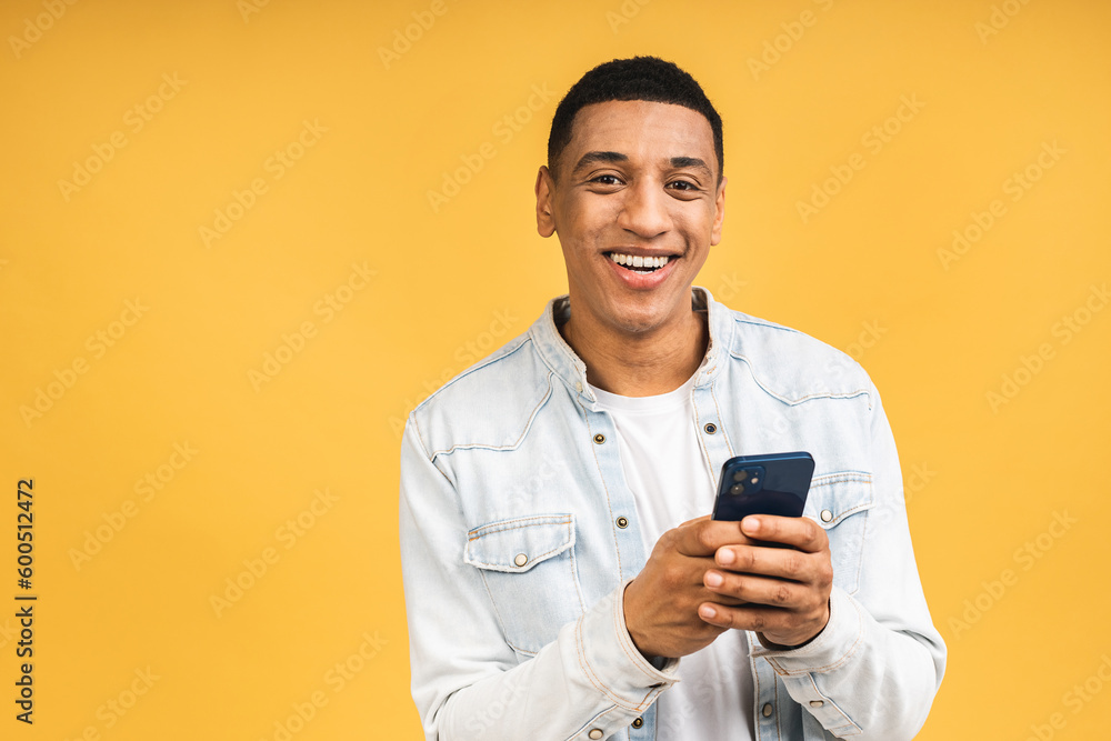 Smiling african american young man holding phone isolated on yellow studio background with copy space aside, african guy using mobile applications, texting. Smiling african american young man holding phone isolated on yellow studio background with copy space aside, african guy using mobile applications, texting.