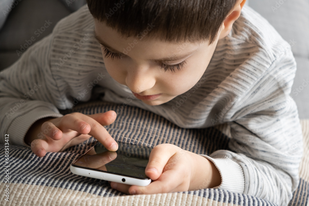 The child uses the phone, holds the smartphone in his hand and looks at the screen. Screen Time, Parental Controls The child uses the phone, holds the smartphone in his hand and looks at the screen. Screen Time, Parental Controls