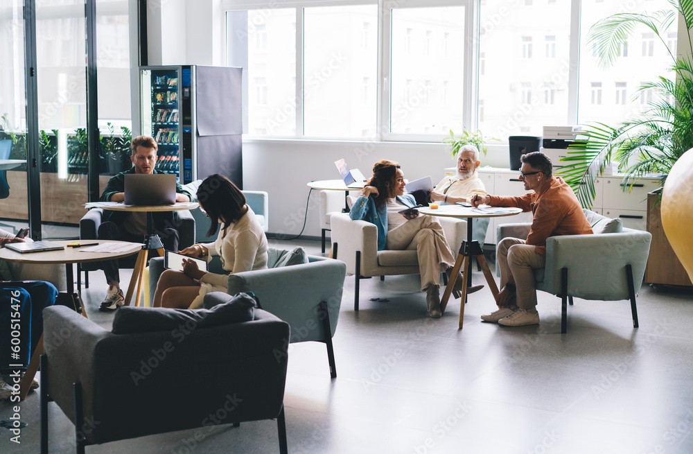 Group of experienced male and female people doing job in involved coworking space using modern technology for web research, multicultural employees talking and browsing wireless - multitasking