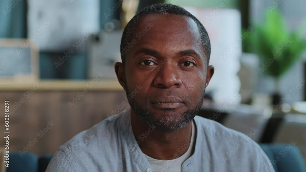 Horizontal close-up portrait of relaxed African American man in living room focused directly at camera. Shot of confident freelancer on blurred background of modern apartment. Daytime. Home interior Horizontal close-up portrait of relaxed African American man in living room focused directly at camera. Shot of confident freelancer on blurred background of modern apartment. Daytime. Home interior