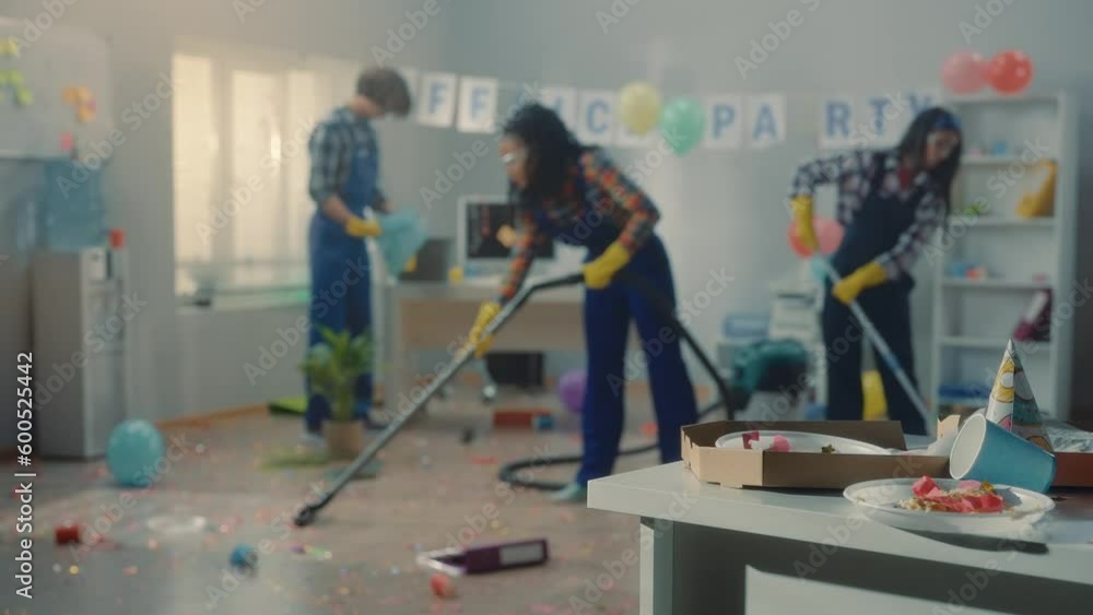 Group of cleaners clean up the office after a corporate party. An African American woman, an Asian woman and a European man mop floors, vacuum and collect garbage in a trash bag. Group of cleaners clean up the office after a corporate party. An African American woman, an Asian woman and a European man mop floors, vacuum and collect garbage in a trash bag.