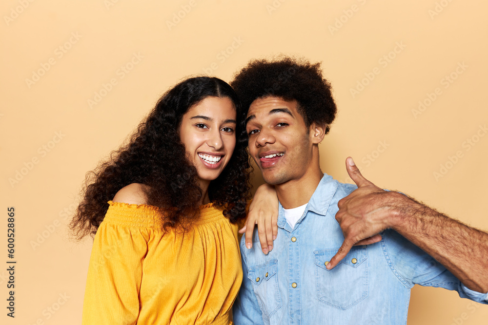 Lovely young african american couple posing against brown background, female leaning her hand on male's shoulder, smiling while guy showing tongue and give me a call gesture with hand and fingers Lovely young african american couple posing against brown background, female leaning her hand on male's shoulder, smiling while guy showing tongue and give me a call gesture with hand and fingers