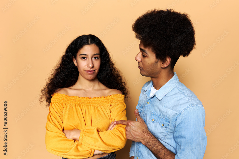 Dissatisfied boyfriend pointing at his girlfriend, accusing her, blaming for mistakes, girl with dark skin and long hair looking at camera with folded arms, ignoring his annoying speech Dissatisfied boyfriend pointing at his girlfriend, accusing her, blaming for mistakes, girl with dark skin and long hair looking at camera with folded arms, ignoring his annoying speech