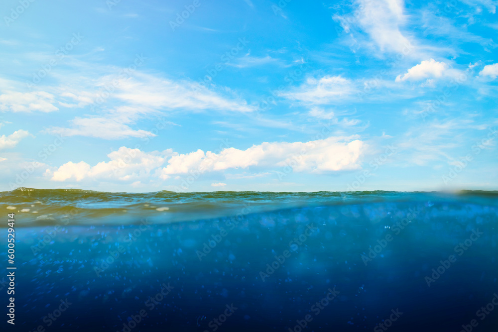 The surface of the sea with the underwater part. Empty space underwater with calm waves and blue sky. Template on the theme of marine tourism.