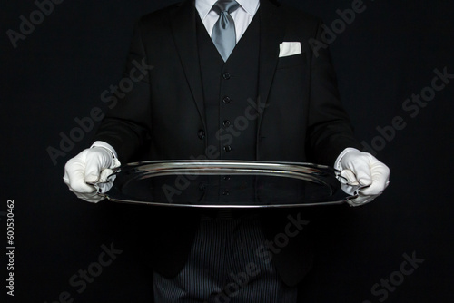 Portrait of Elegant Butler in Dark Suit and White Gloves Holding Large Silver Serving Tray. Service Industry and Professional Hospitality. photo