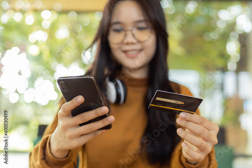 Happy young asian woman holding credit card and mobile phone for electronic payment in internet online remote store.