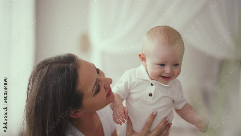 Portrait of active happy cute laughing smiling baby boy at home with mother. Babyhood, childhood motherhood parenting. Mom is babysitting in maternity leave. Raising child, kid and babycare concept. Portrait of active happy cute laughing smiling baby boy at home with mother. Babyhood, childhood motherhood parenting. Mom is babysitting in maternity leave. Raising child, kid and babycare concept.