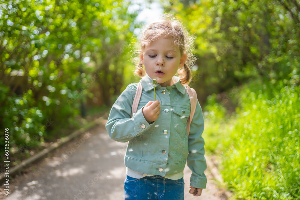 Portrait of happy girl. Child is smiling in spring day. Kid is enjoying spring. Sunny day. Blonde girl is blowing dandelion. Outdoor, close up. Portrait of happy girl. Child is smiling in spring day. Kid is enjoying spring. Sunny day. Blonde girl is blowing dandelion. Outdoor, close up.