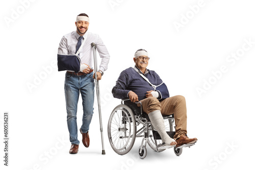 Young man with a broken arm and bandage on head leaning on a crutch and a mature man in a wheelchair