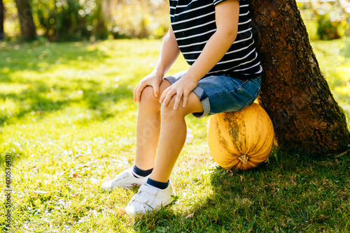 Cute little boy sitting on big yellow ripe pumpkin under traa on the rural garden. Eco sustainable ecology organic farm food harvest concept. photo