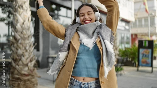 Young beautiful hispanic woman listening to music and dancing at coffee shop terrace