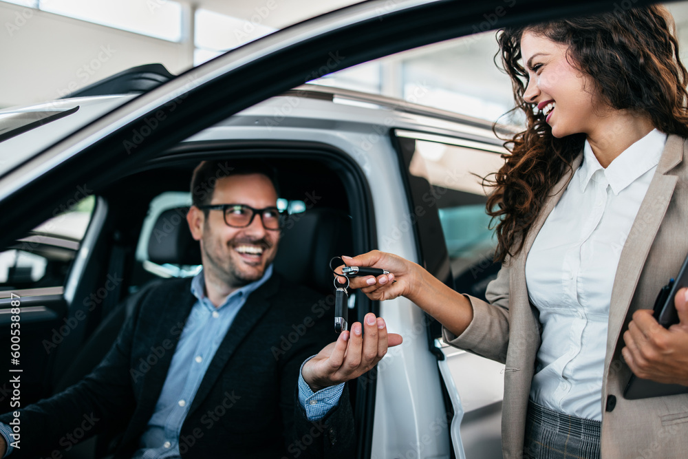 Happy middle age businessman buying new and expensive car. Beautiful female dealer helps him to make right decision. Happy middle age businessman buying new and expensive car. Beautiful female dealer helps him to make right decision.