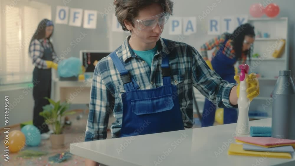 A young male cleaner splashes a spray on the table and wipes the dust. The worker wipes the table with a rag and checks the cleanliness with a finger. Office cleaning after party. A young male cleaner splashes a spray on the table and wipes the dust. The worker wipes the table with a rag and checks the cleanliness with a finger. Office cleaning after party.